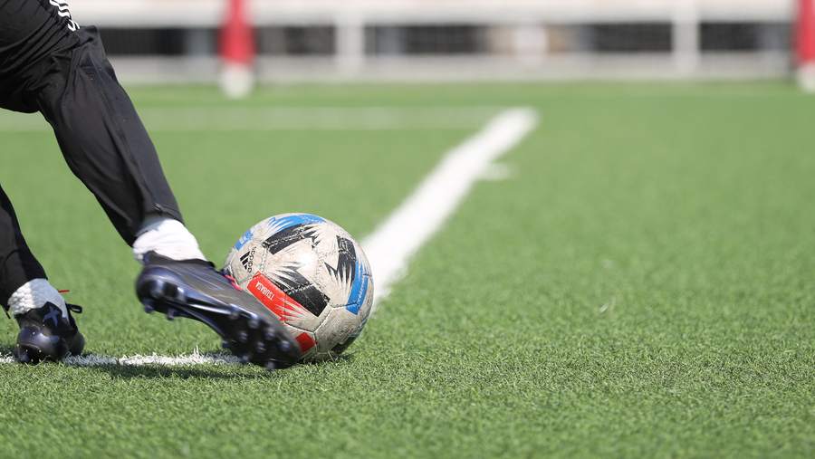 Close view of a boot striking the ball, plant foot beside it on the turf